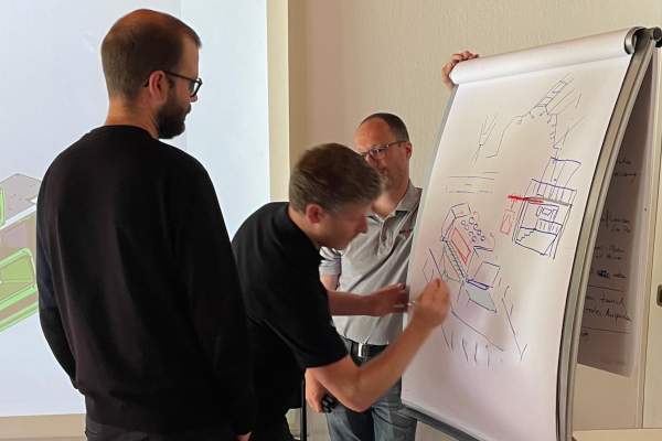 Three Engineers Developing Initial System Design for M 8K at Flip Chart